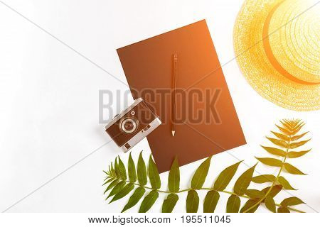Straw hat with green leaves and old camera on white background, Summer background. Top view. Copy space. Still life. Flat lay. Sun flare