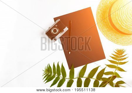 Straw hat with green leaves and old camera on white background, Summer background. Top view. Copy space. Still life. Flat lay. Sun flare
