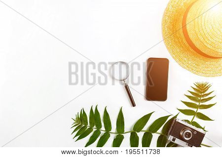 Straw hat with green leaves and old camera on white background, Summer background. Top view. Copy space. Still life. Flat lay. Sun flare