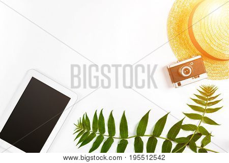 Straw hat with green leaves, tablet and old camera on white background, Summer background. Top view. Copy space. Still life. Flat lay. Sun flare