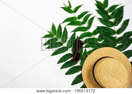 Green leaf branches and straw haton white background. flat lay, top view. Copy space. Still life