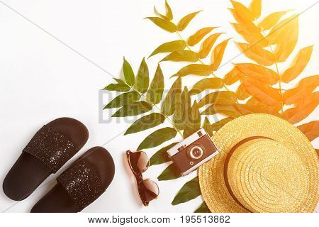 Straw hat with green leaves and old camera on white background, Summer background. Top view. Copy space. Still life. Flat lay. Sun flare