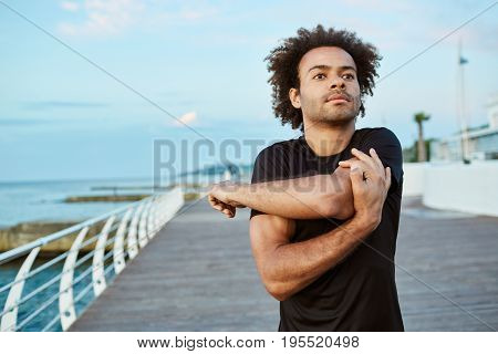 Sports, fitness and healthy lifestyle. Fit young Afro American man doing warm-up before running on the boardwalk in the morning.
