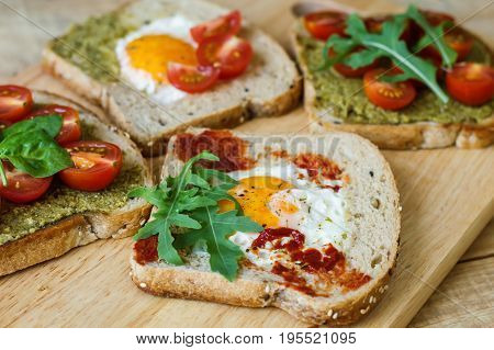 Toasts with egg pesto and tomato sauce arugula spinach cherry tomato and multi cereal bread on wooden background. Healthy breakfast. Balanced meal