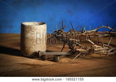 Communion cup with crown of thorns and nails over wooden table over blue background