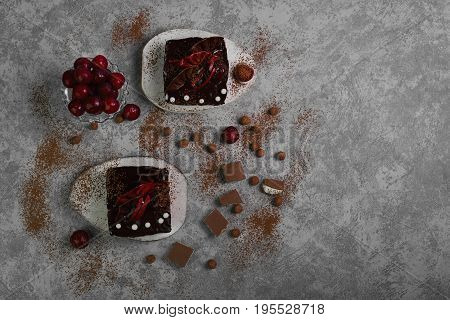 Chocolate cheesecake layered brownies cakes with with dark cherries and cherry sauce. Ingredients for Chocolate cherries cakes Pieces of chocolate and fresh cherries. Gray stone background. Top view.
