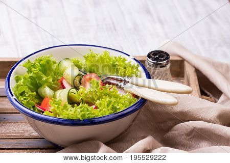 Breakfast in bed. Fresh healthy salad. Tomato, letucce and traditional italian cheese Mozzarella in enamel bowl on wooden tray. Healthy food concept.