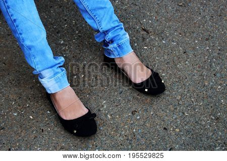 Women's Feet In Blue Jeans And Black Sneakers Close Up