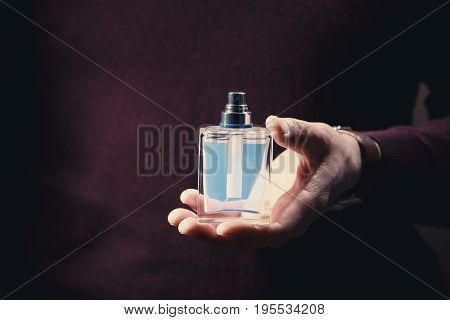 Young man with bottle of perfume, closeup