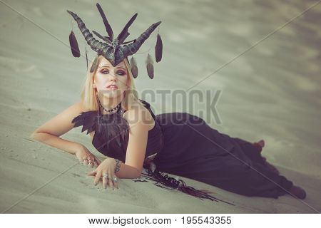 Woman lying on the sand in the desert she has horns on her head.