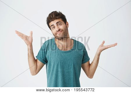 Clueless puzzled attractive and trendy man with widely opened eyes having hesitation shrugging his shoulders expressing uncertainty. Facial expressions, life perception and attitude concept. Nobody cares about it.