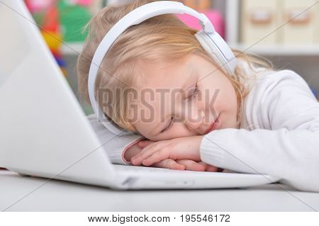 Cute little girl in headphones sleeping near laptop