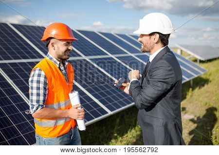 Business client showing photovoltaic detail to foreman. Solar energy station in the field, worker ond order comminicating.