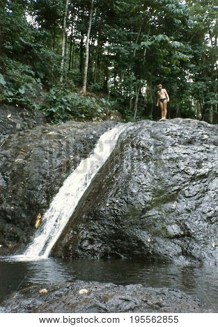 A young man stands atop the Sliding Rocks waterfall on Upolu Island in Samoa.
