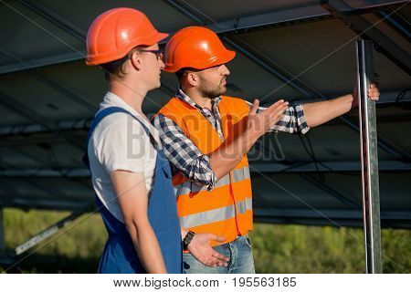 Workers installing photovoltaic panels at solar energy station. Foreman formulating task for employee.