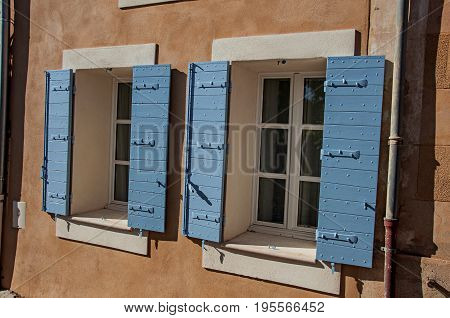 Roussillon, France - July 03, 2016. Detail of windows with blue shutters at sunset in the city center of the village of Roussillon. In the Vaucluse department, Provence region, in southeastern France