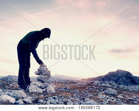 Alone Adult Man Is Stocking Stone To Pyramid.alps Mountain Summit, Evening Sun At Horizon.