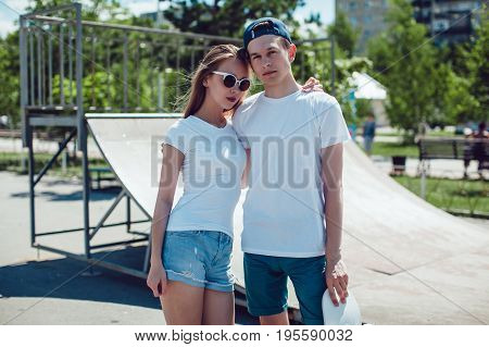 Young couple in white T-shirts posing in skate park. Mock up.