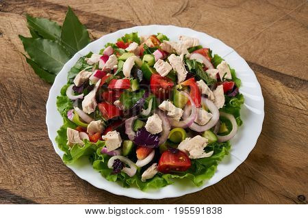 Healthy salad plate with bell pepper tomatoes chicken cucumder onion and mixed greens lettuce parsley on wooden background. Food and health.