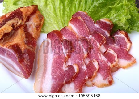 Fresh homemade smoked bacon with leaves lettuce on white plate. Selective focus