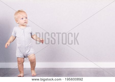 Cute blonde one year kid toddles against the grey background. Copy space.