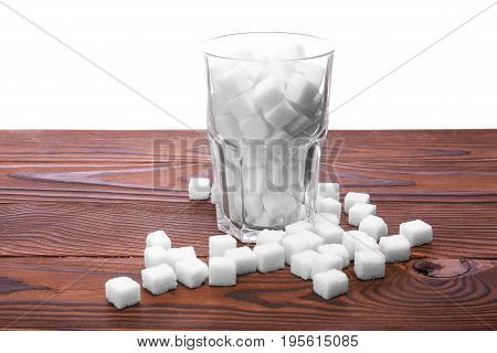 An entire glass of sweet sugar cubes on a table, isolated on a white background. White organic sugar on the dark brown wooden table. Consumption of bad calories.