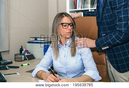 Boss putting hand over shoulder of blonde secretary in the office. Sexual harassment at work concept.