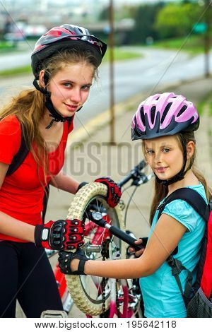 Bicycle tire pumping and repair by child bicyclist on road . Girl wearing bicycle helmet with hand pump . Kids pump up tire. Children return home from school on bicycles.