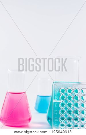 research, science and clinic background. 96 well micro plate and  laboratory beakers with colorful liquids and reagents.