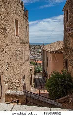Alley with houses, staircase on the slope and blue sky in Haut-de-Cagnes, a pleasant village on top of a hill, near Nice. In the Alpes-Maritimes department, Provence region, southeastern France.