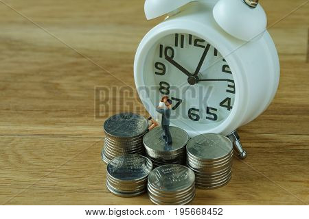selective focus on white alarm clock with stack of coins and miniature couple as financial and time concept.