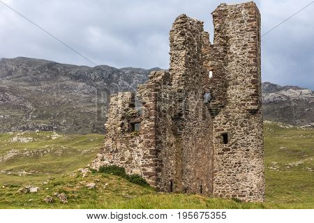 Assynt Peninsula Scotland - June 7 2012: Closeup of brownish Ruins of Castle Ardvreck at Loch Assynt. Green ground vegetation. Cloudy sky.