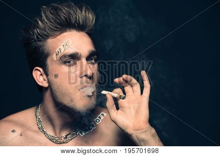 Antisocial behavior, bad habits. Portrait of a bad boy smoking cigarette. Rocker, punk.