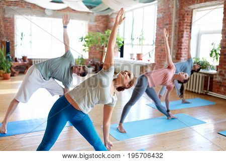 fitness, sport and healthy lifestyle concept - group of people doing yoga in triangle pose at studio