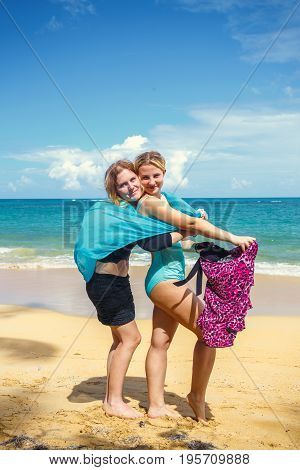 two happy girls with pareos on the sandy beach on background of blue sky