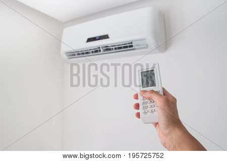 Hand holding remote control, adjusting temperature of air conditioner mounted on a white wall. Indooor comfort temperature