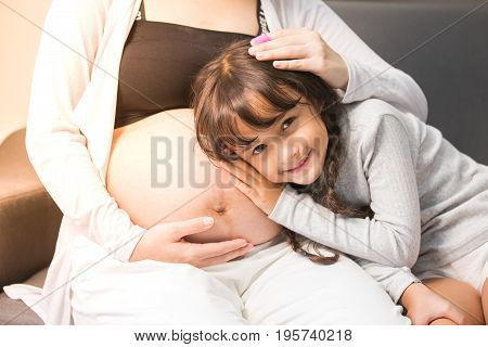 Closeup Of Happy Child Listen To Belly Of Pregnant Woman. Family Having Fun Indoor. Mothers Day Conc