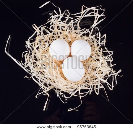 Three chicken eggs in the nest like On a black background
