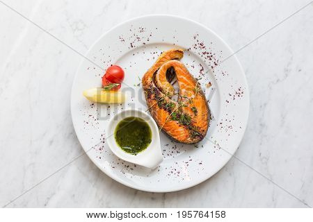Salmon steak with herbs, lemon, tomato and salsa sauce on a plate. top view