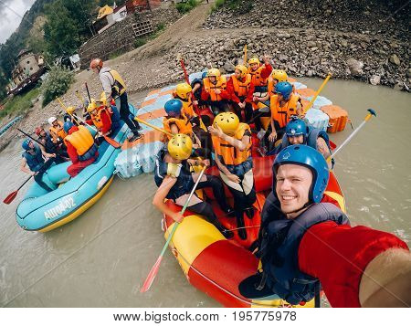 mountain Altai, RUSSIA - July 16, 2017: man in a helmet holds an action camera and makes selfie on the background of friends with oars, rafting