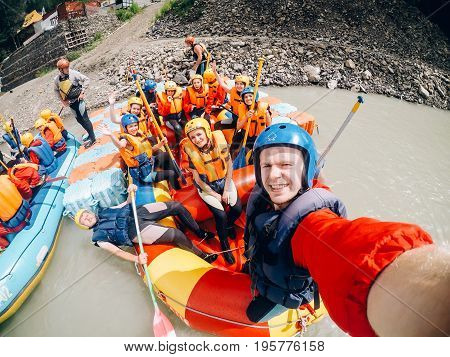 mountain Altai, RUSSIA - July 16, 2017: man in a helmet holds an action camera and makes selfie on the background of friends with oars, rafting