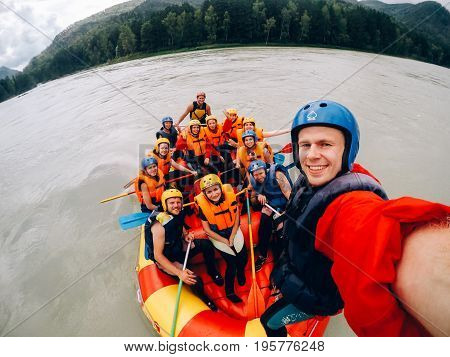 mountain Altai, RUSSIA - July 16, 2017: man in a helmet holds an action camera and makes selfie on the background of friends with oars, rafting