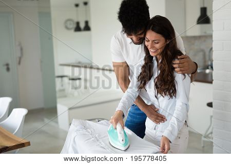 Young happy couple at home doing hosehold chores and ironing