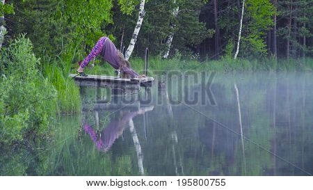 Young woman doing yoga exercises on the lake shore. Artha mukha svanasana
