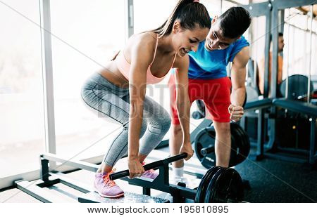 Atrractive woman doing exercises for back with personal trainer in gym