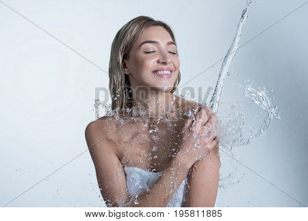 Young happy girl enjoying water stream and splashes falling on her shoulder from above studio shot