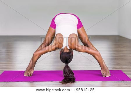 Yoga girl doing wide leg forward fold at gym. Woman stretching legs muscles doing Prasarita Padottanasana training stretches on exercise mat in fitness class.