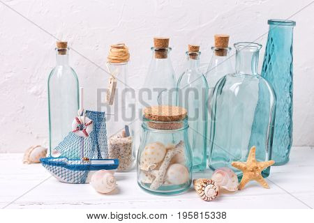 Ocean or sea theme home decorations. Decorative bottles wooden boat starfish shells on white textured background. Selective focus.