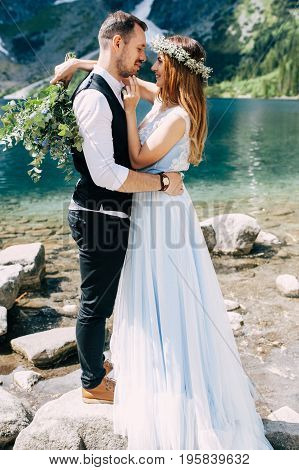 bride with the beautiful blue dress and groom hugging with views of the beautiful green mountains and lake with blue water