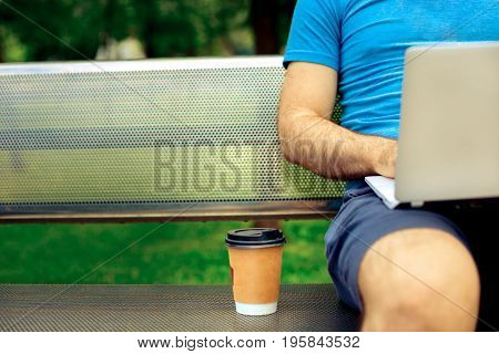 Freelance work. Casual dressed man sitting at wooden beanch inside garden working on computer.